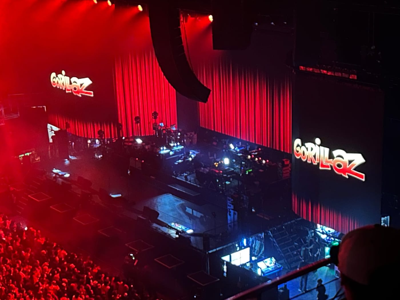 A Gorillaz concert seen from the upper tier, the band name lit up on screens either side of a red-lit stage