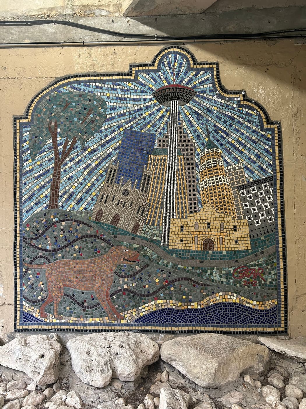A tiled wall mosaic in San Antonio showing the Tower of the Americas, the cathedral and the river, with an animal walking in the foreground